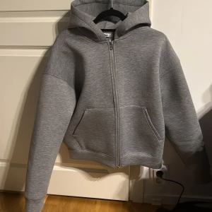 Weekday tröja - Säljer en grå hoodie från Weekday i storlek M. Tröjan har dragkedja framtill, huva och två stora fickor. Oversized passform och mjukt material som känns riktigt skönt. Perfekt för chill dagar eller när du vill ha en enkel och stilren look. Aldrig använd!