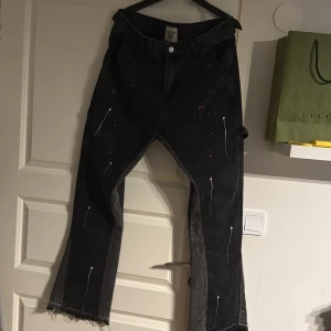 Gallery Dept svarta jeans med färgstänk - Unika svarta jeans från Gallery Dept med färgstänk i vitt, grönt och rött. Byxorna har raka ben, flared nertill och flera fickor på baksidan. Materialet är klassisk denim och designen har en konstnärlig vibe som sticker ut. Passar W32-W34