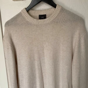 Beige stickad tröja från H&M - Mysig beige stickad tröja från H&M med relaxed fit. Tröjan har rund halsringning, ribbade muddar och är långärmad. Perfekt för lager-på-lager under kyliga dagar.
