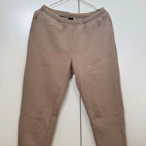 Beige mjukisbyxor från Gina Tricot - Beiga mjukisbyxor från Gina Tricot med resår i midjan och sidofickor. Byxorna är tillverkade i mjukt bomullsmaterial och har en avslappnad passform som är perfekt för chill dagar. Insidan är fleecefodrad för extra komfort.