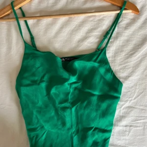Grön satintopp från Zara - Snygg grön satintopp från Zara med tunna justerbara axelband och lätt draperad halsringning. Toppen har en slät och mjuk yta som ger en fräsch look, perfekt till vita jeans eller kjol. Enkel och stilren design som är lätt att matcha.