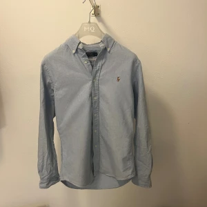 Ljusblå skjorta från Polo Ralph Lauren - Klassisk ljusblå skjorta från Polo Ralph Lauren i slim fit-modell. Skjortan har button down-krage, långa ärmar och knappar framtill. Broderad logga på bröstet och tillverkad i mjuk bomull. Inga fläckar eller liknande så skjortan är i väldigt bra skick. Hör av dig ifall du vill ha fler bilder eller undrar över något! 😊