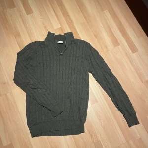 Olivgrön kabelstickad tröja John Henric half zip - Säljer en olivgrön kabelstickad tröja från John Henric med hög krage och half zip-dragkedja. Tröjan är långärmad och har ribbade muddar vid ärmslut och nederkant. Perfekt för lager-på-lager under hösten och vintern. 