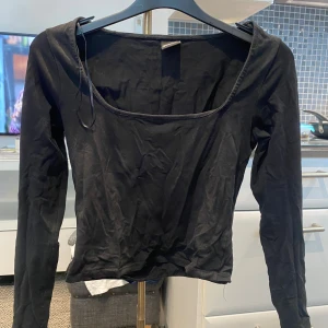 Svart långärmad topp Gina Tricot XS - Svart långärmad topp från Gina Tricot i storlek XS. Modellen har en fyrkantig urringning och är figurnära med croppad passform. Tillverkad i mjuk bomull som är skön mot huden. Perfekt att styla med jeans eller kjol för en clean look.