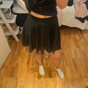 Svart kortkjol med dragkedja - Svart, flowy kortkjol med lätt vidd och diskret dragkedja i sidan. Kjolen har en enkel och stilren design som passar perfekt till många olika looks. Materialet känns lätt och följsamt, vilket ger ett snyggt fall.