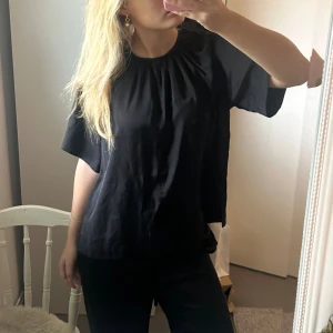 Svart loose blus med v-ringning - Säljer en svart blus med lös passform och korta ärmar. Blusen har en rundad hals med lätt rynkning och en diskret v-ringning framtill. Materialet känns mjukt och har ett snyggt fall, perfekt för en chill och stilren look. Från Wera i stl 38❤️