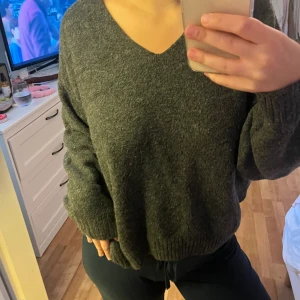 Mörkgrå stickad v-ringad tröja - Mysig mörkgrå stickad tröja med v-ringning och långa ärmar. Tröjan har en relaxed passform och ribbade muddar vid ärmslut och nederkant. Perfekt för kyliga dagar och enkel att styla med dina favoritjeans eller mjukisbyxor.