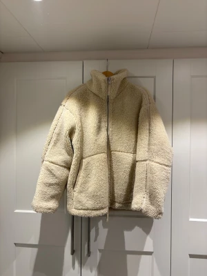 Beige teddyjacka från H&M - Denna populära ocj mysig teddyjacka från H&M i vit färg med hög krage och dragkedja framtill. Köpt för 2 år sedan och sålde slut snabbt.