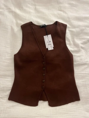 Brun knitted vest Gina Tricot - Helt ny och prislappen kvar alltså jättebra skick!! Ordinarie pris: 300kr. Snygg brun stickad väst med v-ringning och knappar hela vägen framtill. Modellen är figurnära med en liten slits nedtill. Perfekt att styla över en t-shirt eller som den är. Enkel och stilren design som ger en cool vibe.