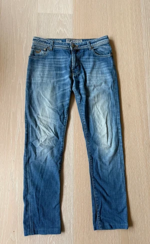 Blå jeans från Jacob Cohen, straight fit, strl 15y/170cm - Snygga blå jeans från Jacob Cohen med klassisk femficksdesign och ljusa slitningar framtill och baktill. Modellen har rak passform, låg midja och detaljerade sömmar på bakfickorna. Materialet är mjukt jeans med dragkedja och knapp framtill.