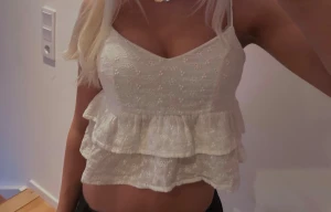 Vit blommig volang linnetopp - Supersöt vit linnetopp med broderade små blommor och dubbla volanger. Toppen har smala axelband, v-ringad hals och är croppad för en fräsch sommarkänsla. Perfekt att styla med jeans eller kjol för en chill look.