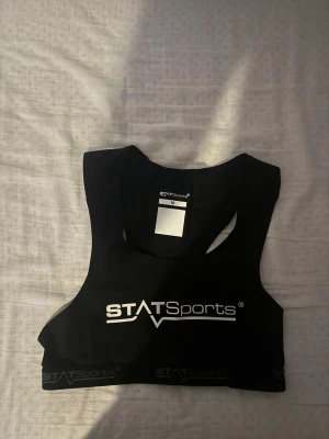 Svart tränings vest från STATSports - Sportig svart  från STATSports med vitt logotryck framtill och elastisk kant med logga. Toppen är ärmlös och har en meshpanel på ryggen med ficka för GPS eller sensor. Perfekt för träning och fotboll.  GPS INGÅR INTE! Kom med bud.