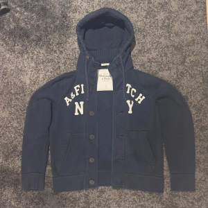 Mörkblå Abercrombie & Fitch kofta, cardigan, hoodie med knappar - Säljer denna Abercrombie and Fitch hoodien med knappar, den är väldigt fint skick och jag ser personligen inga defekter eller skador. Storlek L men passar även bra för mig som har M. Mer bilder/info kan fås i DM.