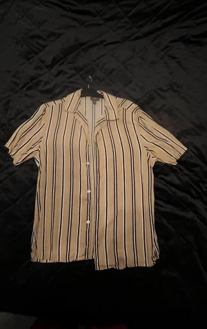 Beige och svart randig skjorta - Snygg kortärmad skjorta från H&M i beige med svarta och vita vertikala ränder. Storleken är M.