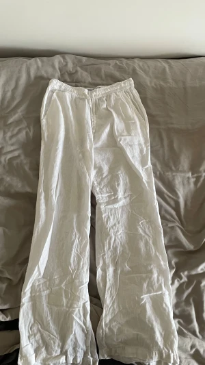 Vita linnebyxor med resårmidja - Säljer ett par vita linnebyxor med skön resår i midjan och raka, vida ben. Byxorna har fickor på sidorna och är perfekta för varma dagar. Materialet är lätt och luftigt linne, vilket gör dem riktigt bekväma och stilrena.