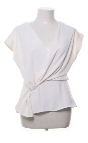 Vit omlott blus med knyt - Säljer en stilren vit blus med omlott-design och snygg knytning i sidan. Toppen har korta ärmar och ett mjukt, flowigt tyg som ger en chill och modern vibe. Perfekt för dig som gillar minimalistisk stil och vill ha något som sticker ut med sin coola omlott-look.
