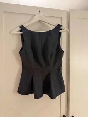 Grå ärmlös topp med öppen rygg - Snygg grå topp med breda axelband och figurnära passform. Toppen har en cool öppen rygg och en diskret dragkedja i sidan för enkel påklädning. Materialet är mjukt och har en lätt struktur, perfekt för att ge en stilren vibe.