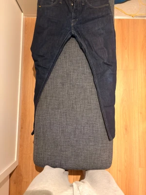 Mörkblå jeans från Tiger of Sweden - Snygga mörkblå jeans från Tiger of Sweden med klassisk femficksdesign och kontrastsömmar. Jeansen har raka ben och normal passform, tillverkade i slitstarkt denim med diskret läderpatch bak i midjan. Perfekta för dig som gillar stilrena och tidlösa jeans.