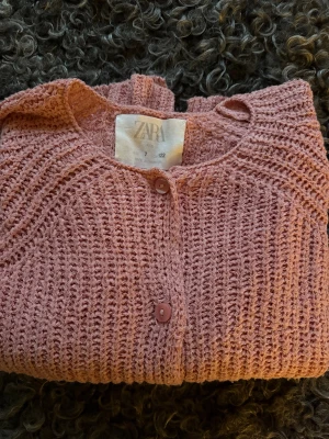 Gammelrosa stickad kofta från Zara - Säljer en söt rosa stickad kofta från Zara med ribbad struktur och rund hals. Koftan har långa ärmar och stängs med matchande rosa knappar framtill. Perfekt för dig som gillar mjuka och mysiga plagg med enkel design, snyggt till både klänning och jeans.