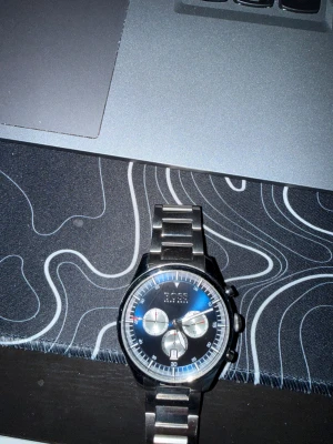 Hugo Boss kronograf klocka i stål - Snygg kronografklocka från Hugo Boss med blå urtavla och silverfärgade detaljer. Länken är i rostfritt stål och boetten har en rund form. Klockan har tre subdials, datumvisning och tydliga markeringar runt urtavlan. Perfekt accessoar för dig som gillar stilren design.