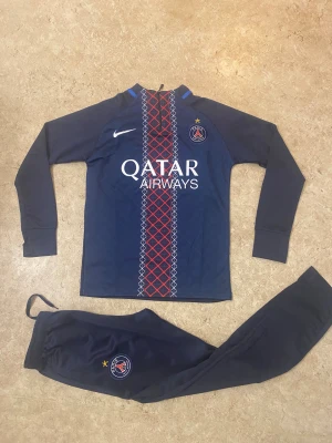 PSG långärmad fotbollströja Nike - Paris Saint-Germain långärmad fotbollströja från Nike i mörkblått med rött och vitt randigt mönster längs mitten. PSG-logga och Qatar Airways-tryck på bröstet. Tillverkad i mjukt, funktionellt material som andas. Perfekt för dig som vill representera PSG på träning eller match.