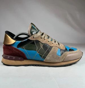 Valentino Garavani Rockrunner sneakers - Säljer ett par Valentino Garavani Rockrunner sneakers med camouflagemönster i blått, grönt och beige. Skorna har detaljer i mocka, skinn och textil, samt guld- och vinröda inslag vid hälen. Platt sula och snörning framtill. Perfekt för dig som gillar statement-sneakers.