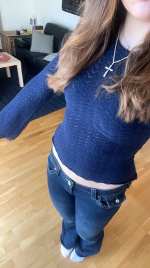 Mörkblå stickad topp från AWARE - Säljer en mörkblå, stickad topp från AWARE i storlek M. Tröjan har långärmad passform, är croppad och har ett snyggt hålmönster i zigzag. Materialet är mjukt och stretchigt, perfekt för dig som gillar en lite mer slim fit look.