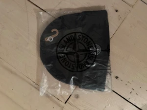 Svart mössa från Stone Island - Svart mössa från Stone Island med klassisk logotyp framtill. Snygg och enkel design som passar till de flesta stilar. Materialet är stickat och mössan är perfekt för kyliga dagar. Kommer i originalförpackning.