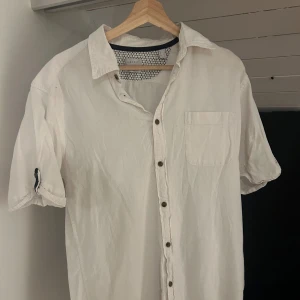 Vit kortärmad skjorta från Esprit - Vit skjorta från Esprit i bomull med korta ärmar, klassisk krage och bröstficka. Skjortan har knappar framtill och en avslappnad passform. Perfekt för en clean och enkel stil.