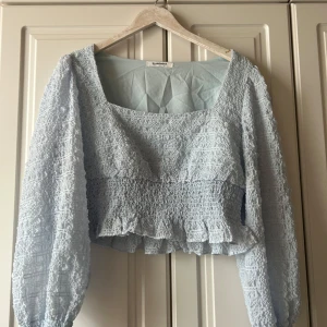 Ljusblå croppad blus från Glamorous - Supersöt ljusblå blus. croppad passform, långa puffärmar och smockad struktur. Fyrkantig ringning och volangdetalj nedtill.