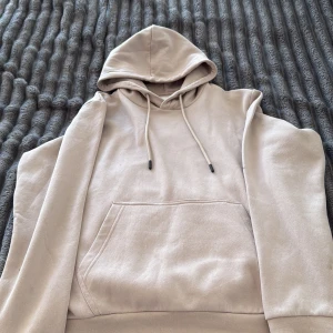 Beige hoodie från Jack & Jones - Säljer en stilren beige hoodie från Jack & Jones med huva och snörning. Tröjan har en klassisk känguruficka framtill och ribbade muddar vid ärmslut och nederkant. Perfekt för dig som gillar en enkel och clean look.