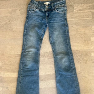 Blå bootcut jeans barn från Gina Tricot! - Snygga blå barn jeans från Gina Tricot i klassisk bootcut-modell. Jeansen har dubbla knappar i midjan, fem fickor och coola detaljer på bakfickorna. Tillverkade i mjukt denimtyg med lätt slitning för en avslappnad look.