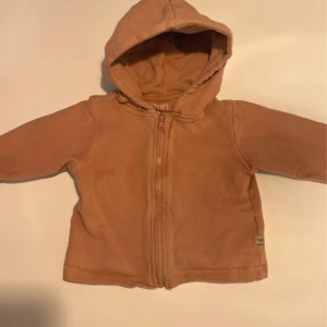 Beige hoodie med dragkedja från BEBE - Mysig beige hoodie från BEBE i mjuk bomull. Tröjan har huva, lång ärm och hel dragkedja framtill. Perfekt för lager-på-lager under kyliga dagar. Enkel och stilren design som passar till det mesta.