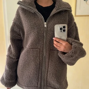 Brun teddyjacka från H&M, storlek M - Mysig brun teddyjacka från H&M i storlek M. Jackan har oversized passform, hög krage och dragkedja framtill. Tillverkad i mjukt fleece-material med stora fickor och breda ärmar. Perfekt för kalla dagar när du vill vara både varm och snygg.