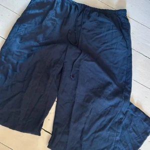 Mörkblå linnebyxor från Gina Tricot - Mörkblå linnebyxor från Gina Tricot med avslappnad passform och resår i midjan. Byxorna har snörning framtill och är tillverkade i ett lätt och luftigt linnematerial, perfekta för varma dagar.