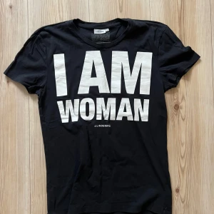 Svart t-shirt J.Lindeberg I AM WOMAN - S - Svart t-shirt från J.Lindeberg med stort vitt tryck 'I AM WOMAN' på bröstet. Gjord i 100% ekologisk bomull, klassisk passform och rund hals. Perfekt statement-plagg för dig som vill sticka ut.