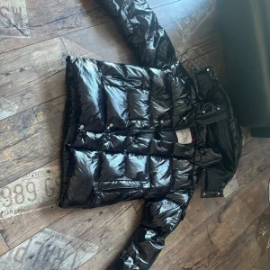 Moncler jacka - Säljer en svart, glansig dunjacka från Moncler med huva och klassisk logga på ärmen. Jackan har några defekter som visas i bilderna men de är bara på insidan har fler bilder så bara höra av sig priset är ej hugget i sten. Säljer för den är lite liten för mig