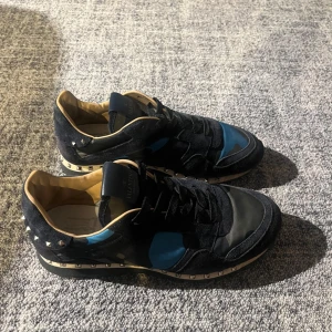 Valentino Rockrunner sneakers svart/blå - Snygga Valentino Rockrunner sneakers i svart mocka och textil med blå och grå detaljer. Skorna har ikoniska nitar runt hälen och sulan, samt svarta skosnören och robust gummisula.  Skick 8/10 med två nittar som saknas, Pris är diskutabelt!