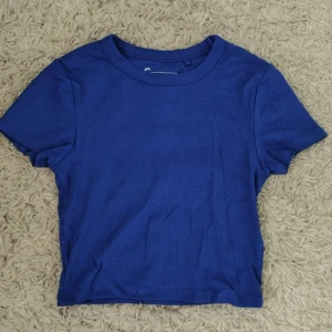 Blå ribbad t-shirt - En enkel blå t-shirt med ribbad struktur och rund hals. Modellen är kortärmad och har en klassisk passform och är lite croppad. Köpt från NewYorker, står storlek S men skulle säga mer som xs.