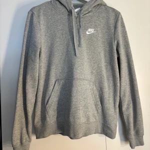 Grå hoodie från Nike med huva - Säljer en grå hoodie från Nike med klassisk logga på bröstet. Tröjan har huva med snörning, stor magficka och långa ärmar. 