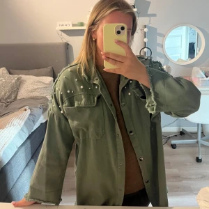 Grön jeansjacka med pärlor - Snygg grön jeansjacka  med pärldetaljer på axlar och överdel. Jackan har fransade kanter vid ärmslut och nederkant, stora bröstfickor och knäppning framtill. Oversized passform. Den är köpt på second hand därav inget märke eller storlek, men jag är 152 som preferens!🩵🩷