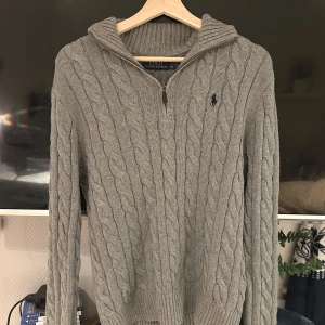 Grå kabelstickad tröja Polo Ralph Lauren - Tröjan är använd endast 1 gång och säljer för att den inte sitter bra längre. Det är en grå Ralph Lauren half zip men ränder, Det finns QR kod för att se så den är riktig.