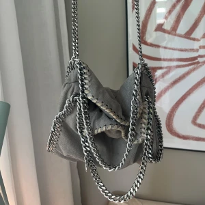 Stella mccartney väska - Säljer min grå stella mccartney väska med rosa insida! Köpt på vestaire collective, självklart äkta! Tecken på använding finns då den är lite smått smutsig på insidan och utsidan, men det är inget som syns när man använder den och det går såklart att tvätta bort☺️Går att ha den crossbody (första bilden) och att hålla i den (tredje bilden) skriv för fler bilder och information❤️ 
