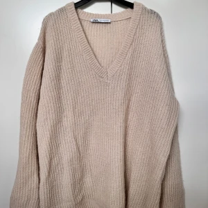 Beige stickad v-ringad tröja Zara - Supermysig beige stickad tröja från Zara med djup v-ringning och lång ärm. Oversized fit som ger en chill vibe, perfekt att slänga på sig när det är kallt. Tjockt, fluffigt material som känns lyxigt och skönt mot huden.