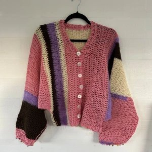 Färgglad handvirkad kofta med knappar - Unik handvirkad kofta i rosa, beige, lila och brunt med stora ballongärmar och vita knappar framtill. Koftan har ett coolt randigt mönster och är gjord i ett grovt stickat material som känns både retro och trendigt. Perfekt för dig som vill sticka ut!🤩💕