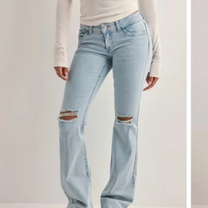 Ljusblå bootcut jeans med slitningar - Snygga ljusblå jeans med bootcut passform och slitna hål på knäna. Jeansen har broderade rosa detaljer på bakfickorna. Endast använda 1-2 gånger så i nyskick, kostar 700kr på hemsidan. 