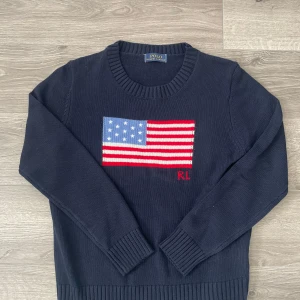 Ralph Lauren USA tröja  - Mörkblå tröja från Ralph Lauren med amerikansk flagga i rött, vitt och blått framtill samt RL-broderi. Klassisk rund halsringning och ribbade muddar vid ärmslut och nederkant. Perfekt för dig som gillar grisch och Old Money stilen. Tröjan är i väldigt bra skick utan fläckar och defekter. Sparsamt använd. Mått finns i annonsen då storlek inte står. Det är bara att höra av dig vid funderingar!✅🤩