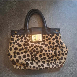 Y2k Leopardmönstrad handväska  - Säljer en snygg handväska med leopardmönster och svarta handtag samt detaljer. Väskan har en innerficka, mobilficka och stängs med ett dekorativt spänne i metall. Tror axelband saknas. Förg stämmer bäst in på första bilden! 🩷Pris går att diskutera.
