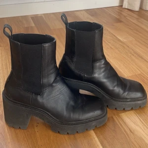 Svarta chunky chelsea boots i skinn - Säljer ett par svarta chelsea boots med chunky sula och låg klack. Skorna har elastiska paneler på sidorna och är tillverkade i skinn. De har en fyrkantig tå och grov yttersula som ger en cool och modern vibe.