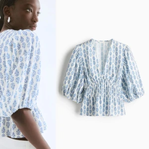 Vit och blå blus med puffärm - Supersöt blus i vitt med blått blommigt mönster och v-ringning. Blusen har puffiga trekvartsärmar och smockad midja som ger en snygg siluett. Perfekt för dig som gillar romantiska och trendiga detaljer.